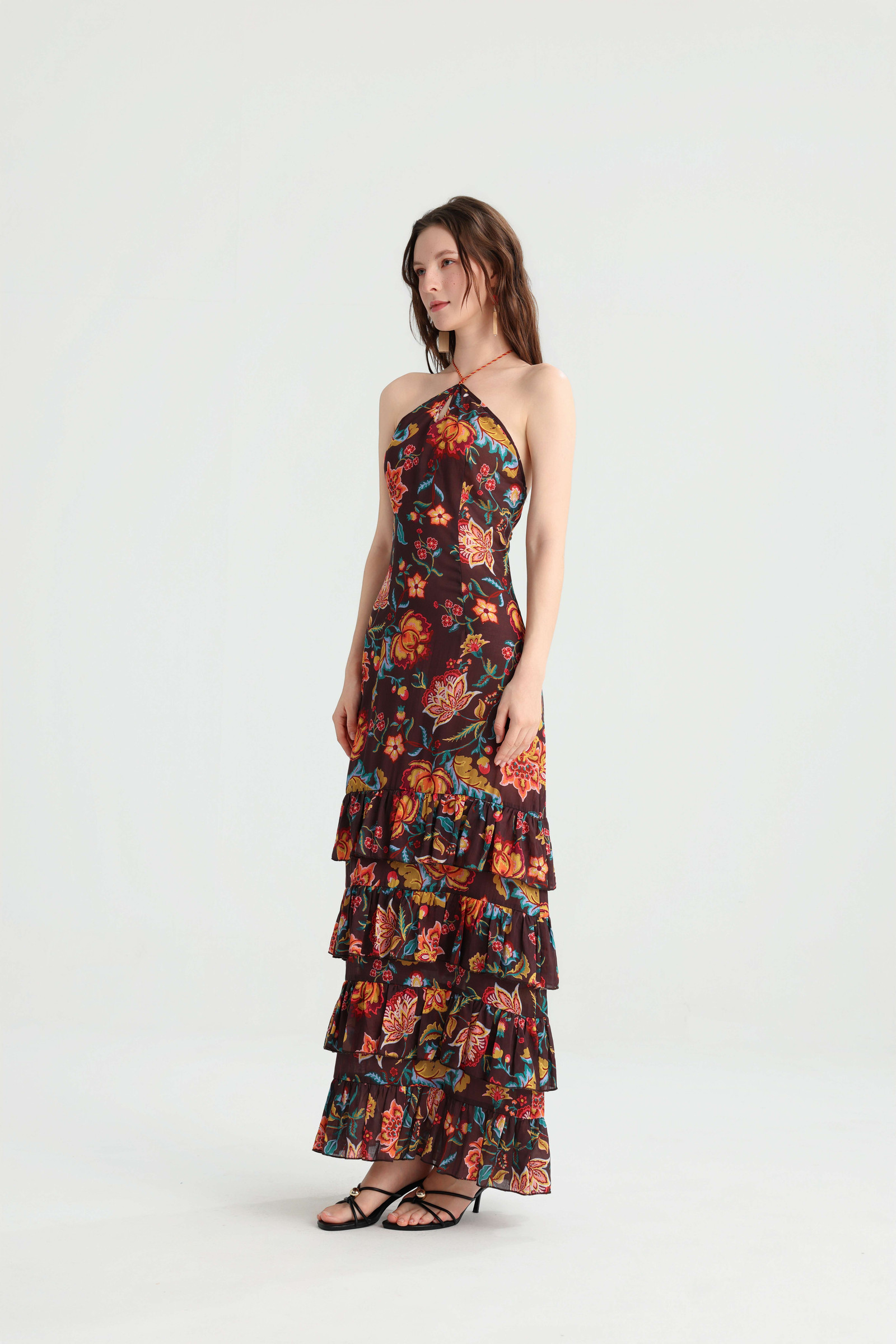 Angled view of the dark brown floral halter dress and its layered ruffle skirt