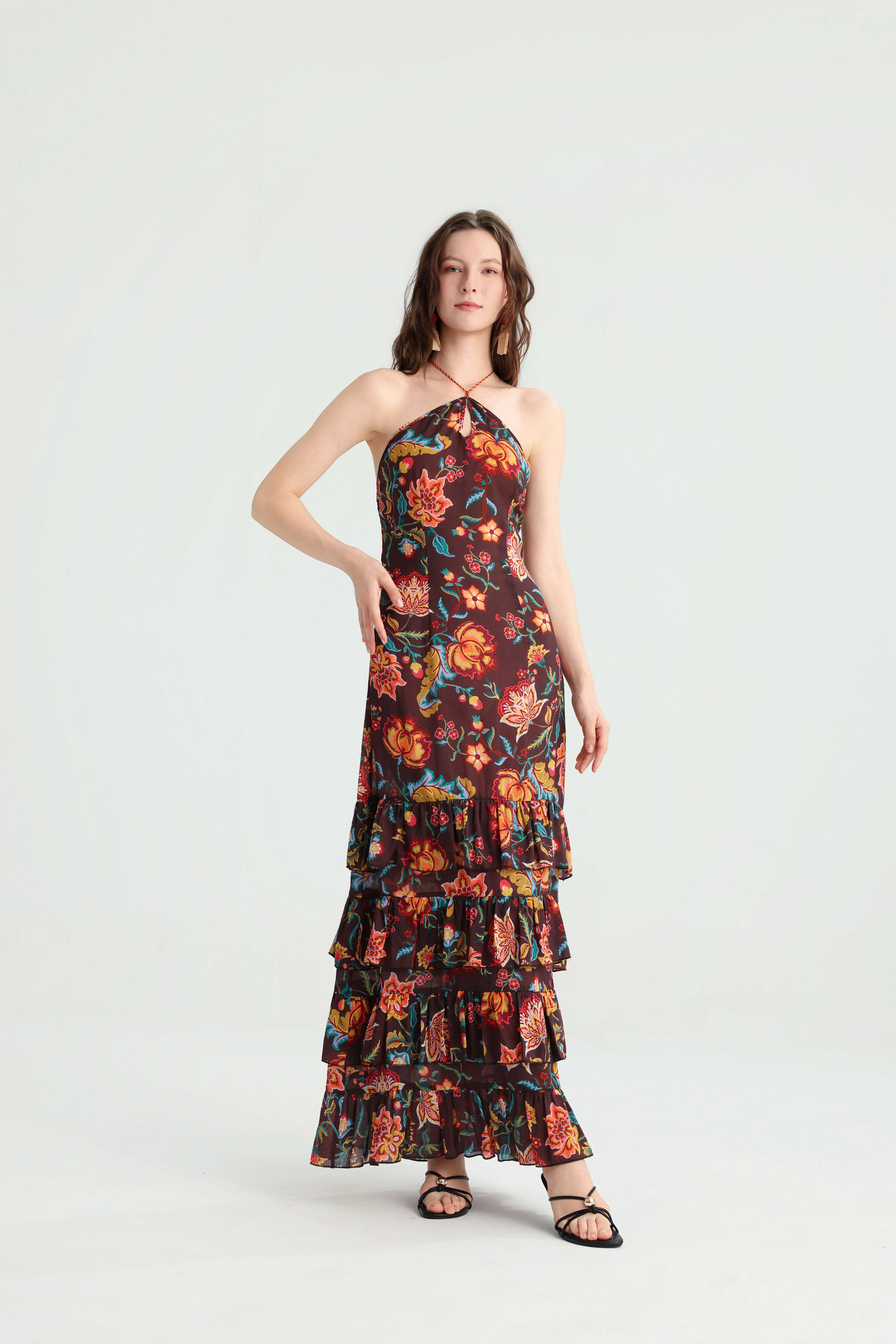 Model posing with one hand on her hip in the dark brown floral halter maxi dress