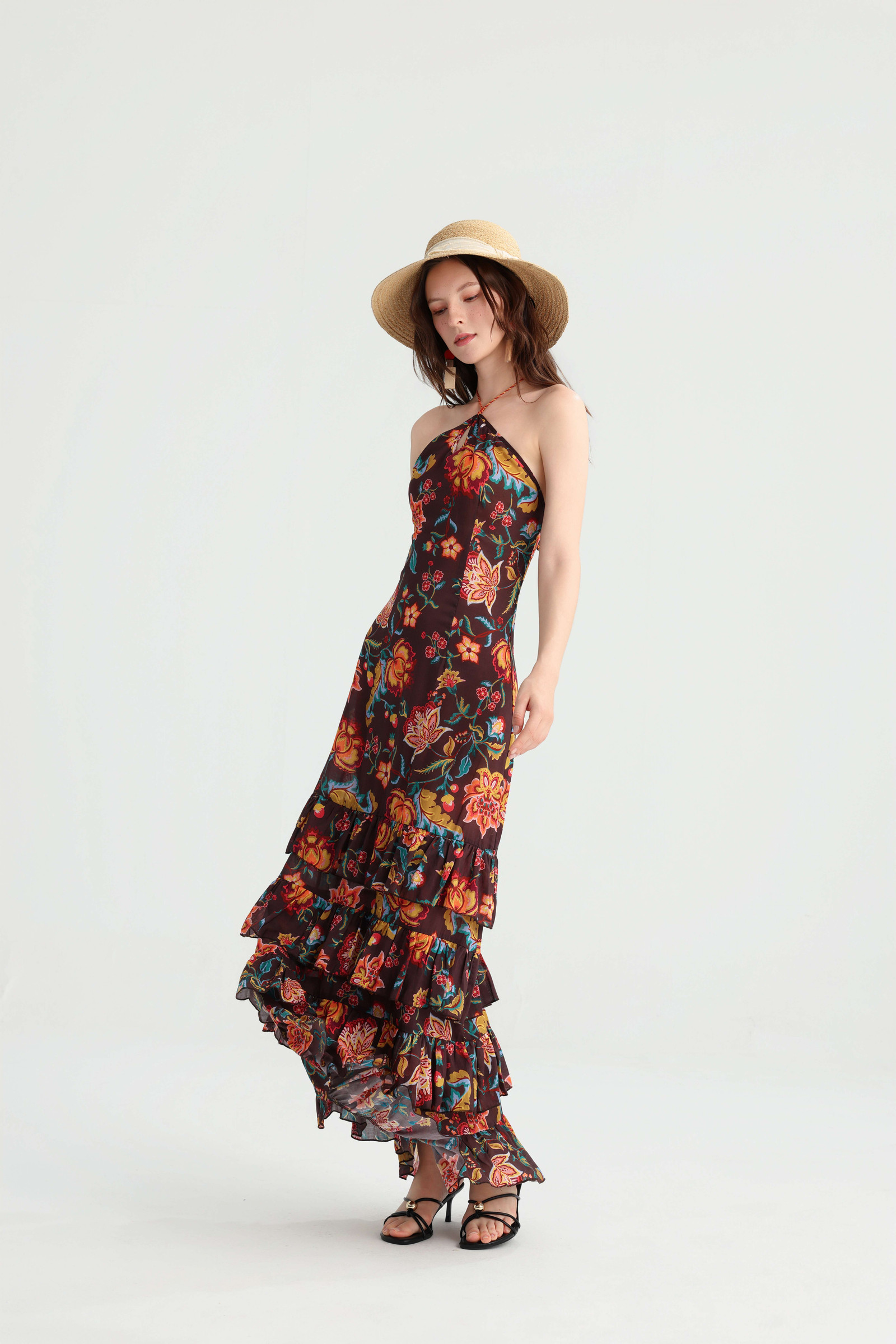 Model wearing the floral halter dress with a straw hat, the tiered ruffle skirt lifted slightly in motion