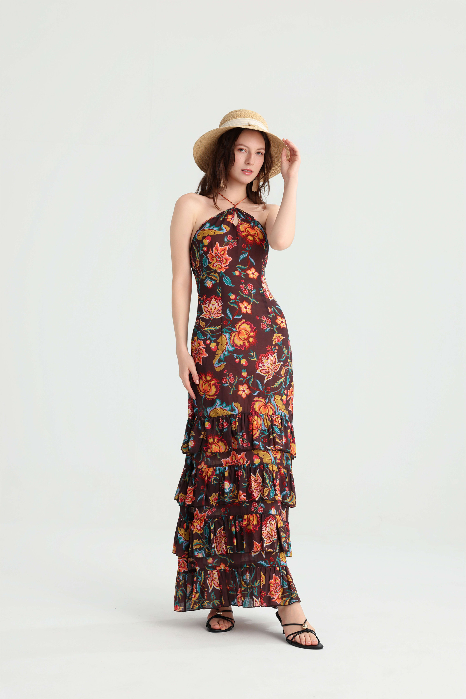 Model touching the brim of a straw hat while wearing the dark brown floral maxi dress