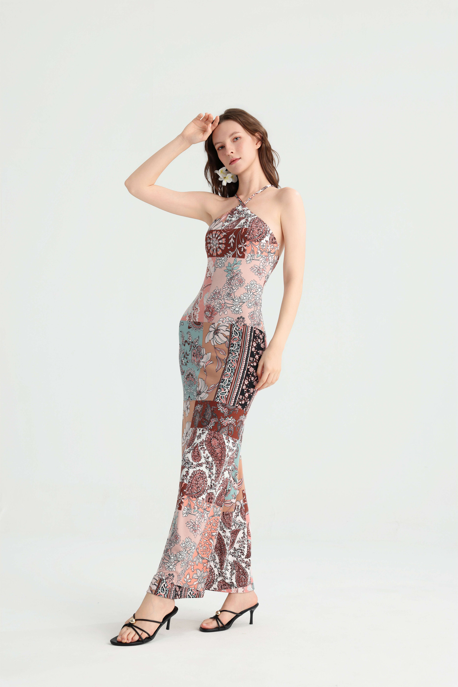 Angled view of the floral patchwork halter dress with the model raising one hand to her forehead